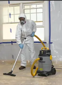 Mold Terminators technician in protective suit operating HEPA vacuum during remediation